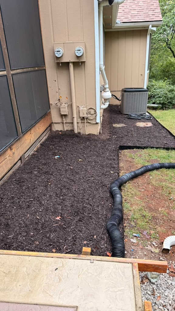 Fresh mulch and landscape edging beside a Mission, KS home with a visible drainage pipe